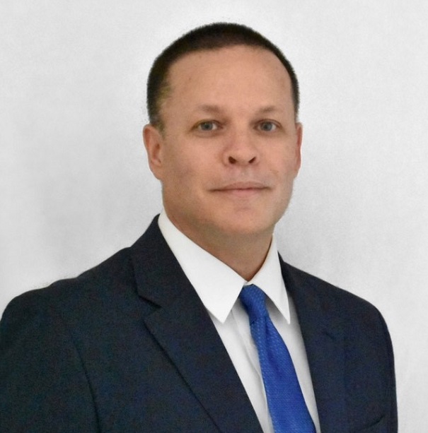 Person in a suit with a blue tie against a plain background.