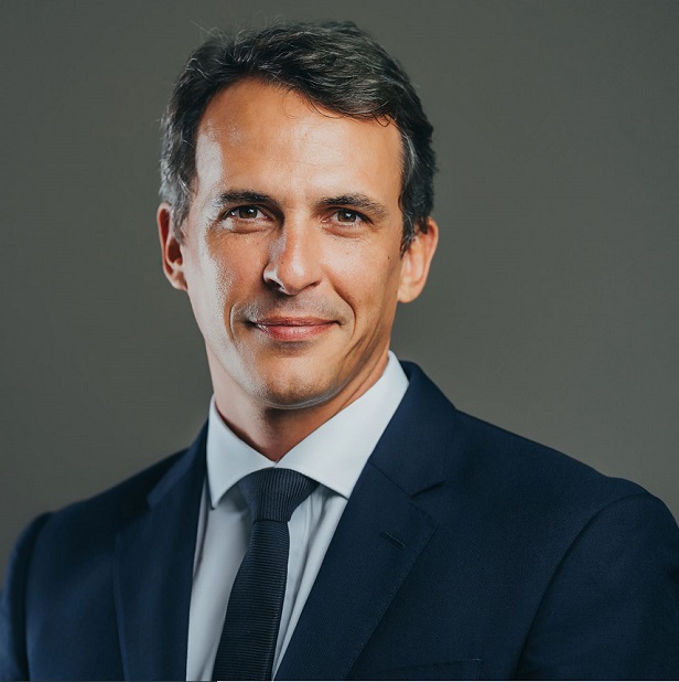 Person in a suit smiling at the camera with a neutral background.