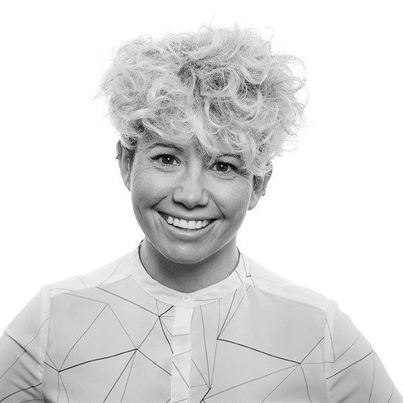 Person smiling with curly hair in a geometric patterned shirt.