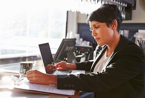 Person working on a laptop at a desk with papers and a cup.