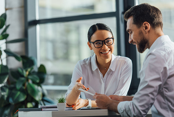 Two people having a discussion at a desk in a bright office with plants.