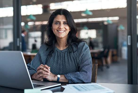 Person smiling at a desk with a laptop in an office setting.