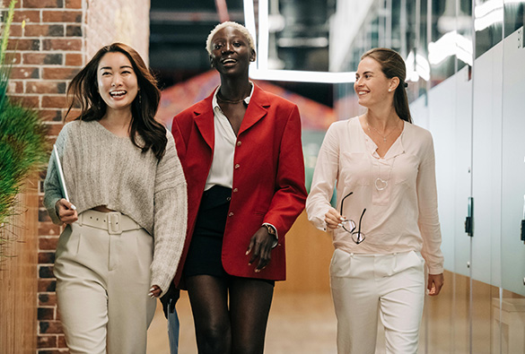 Three people walking and smiling in an office corridor.