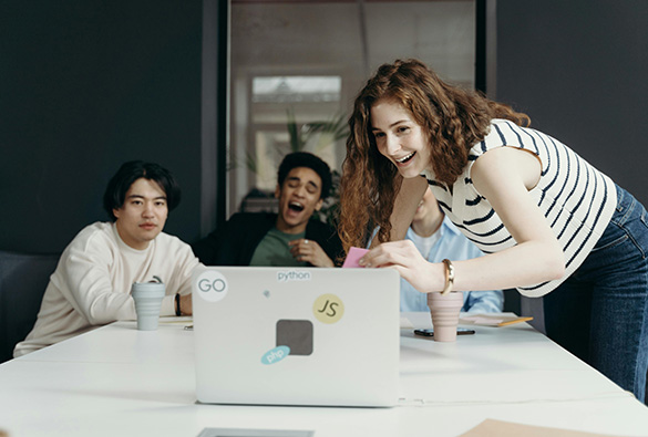 Group of people smiling and working around a laptop with programming stickers.