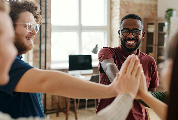Group of people smiling and giving a high five in an office setting.