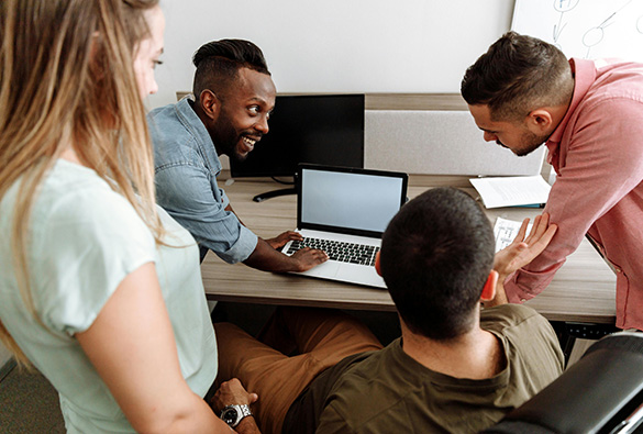 A group of colleagues discussing a project around a laptop in an office.