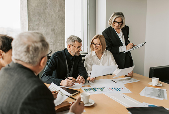 Group of people in a meeting reviewing documents and graphs around a table.