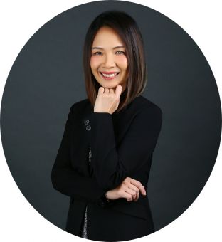 Person in a black suit smiling with hand on chin.