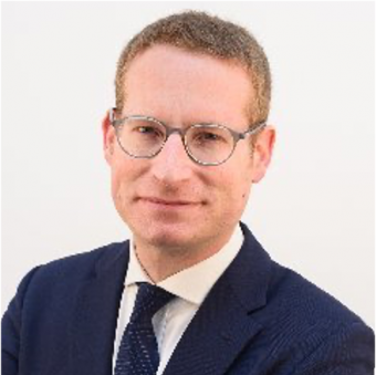 Person wearing glasses and a suit, smiling slightly.