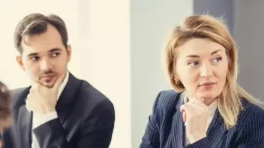 Two people in business attire attentively listening in a meeting.