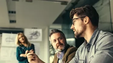 People in a meeting room discussing with papers on wall.