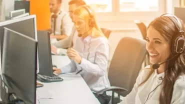Smiling call center agents wearing headsets, working on computers.