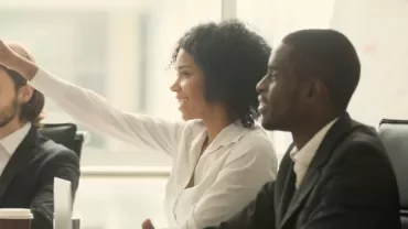 People seated at a meeting table, one raising a hand.