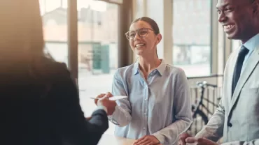 Smiling people at a desk interacting with a receptionist.