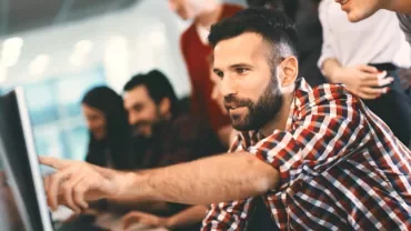 A group of people collaborating at a computer screen in an office setting.