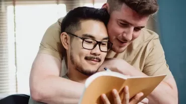 Two people smiling while reading a notebook together in a cozy room.