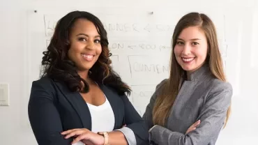 Two professionals smiling, standing in front of a whiteboard.