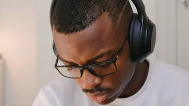 Person wearing headphones and glasses, sitting in a room with a modern lamp.