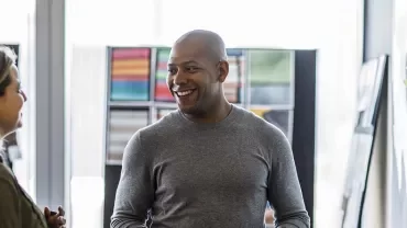 Two people smiling and talking in an office space with colorful artwork on the walls.