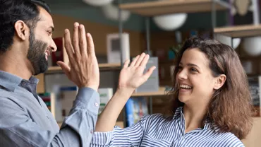 Two people smiling and high-fiving inside an office with bookshelves.