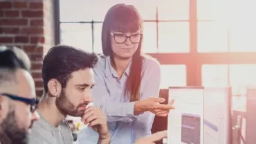 Team collaborating at a computer in a sunlit office.