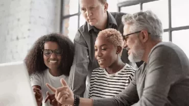 A group of people collaborating around a laptop in a bright room.