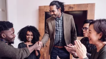 Smiling colleagues clapping as two people shake hands in an office.