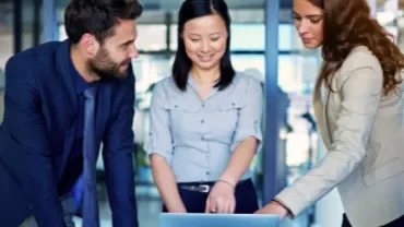 Group discussion around a laptop in a modern office.