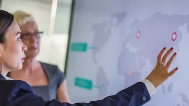 Two people discussing data displayed on a large screen with a world map.