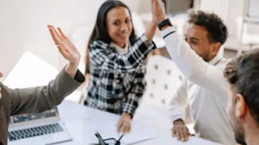 Diverse group of professionals high-fiving in a meeting.