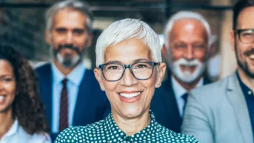 Group of five smiling professionals in office attire.