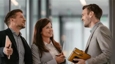 Three people in business attire having a friendly conversation indoors.