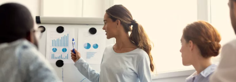 Person presenting data charts on a whiteboard in a meeting room.