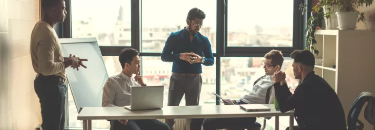 A team meeting in a bright office with five people discussing around a table.