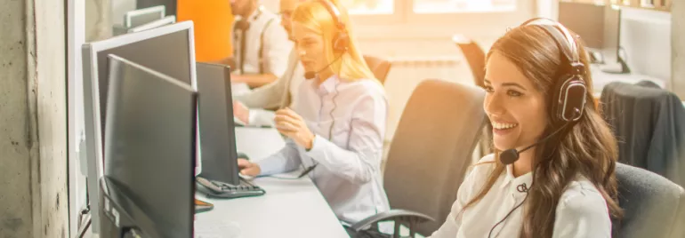 Smiling call center agents wearing headsets, working on computers.