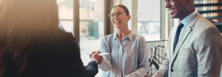 Smiling people at a desk interacting with a receptionist.