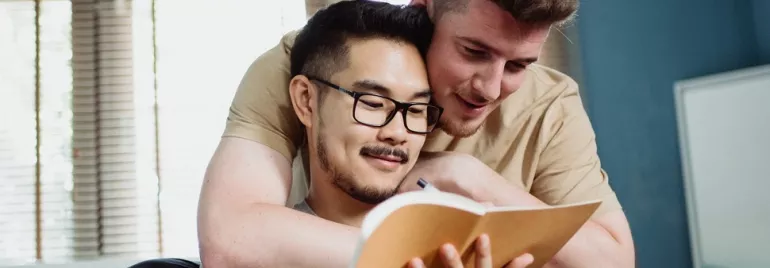 Two people smiling while reading a notebook together in a cozy room.