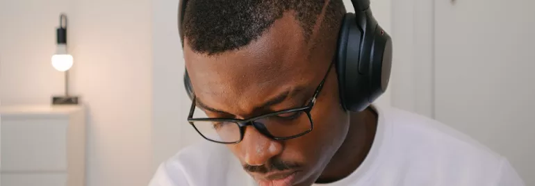 Person wearing headphones and glasses, sitting in a room with a modern lamp.