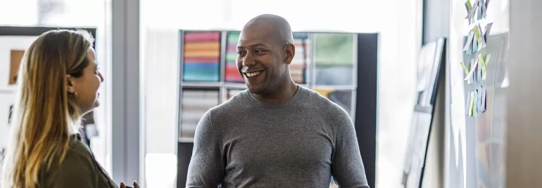Two people smiling and talking in an office space with colorful artwork on the walls.