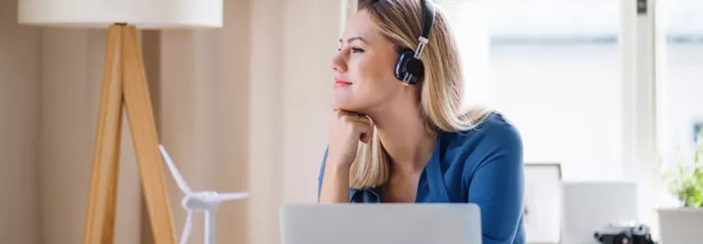 Person with headphones looking out the window, seated at a desk with a laptop.