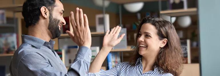 Two people smiling and high-fiving inside an office with bookshelves.