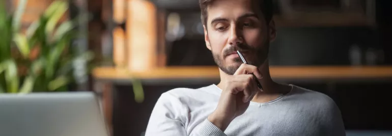 Person thinking while holding a pen, sitting at a desk.