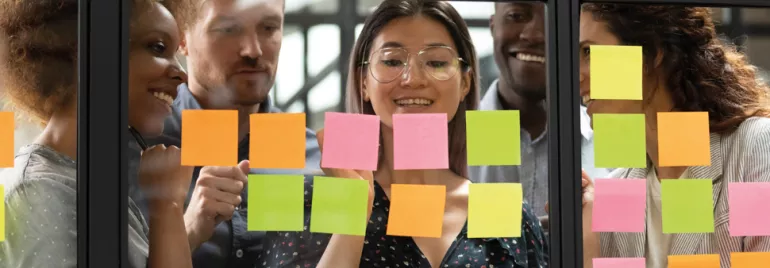 Group of colleagues brainstorming with sticky notes on glass.