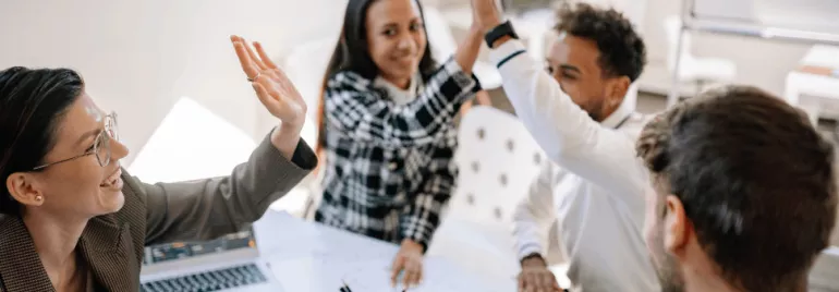 Diverse group of professionals high-fiving in a meeting.