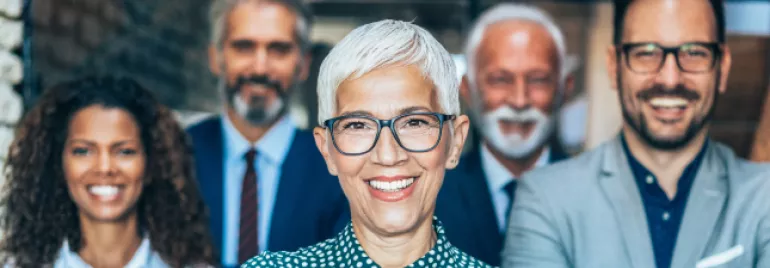 Group of five smiling professionals in office attire.