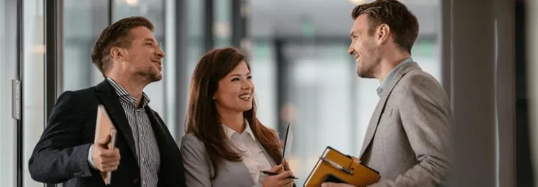 Three people in business attire having a friendly conversation indoors.