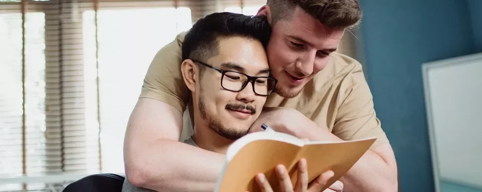 Two people smiling while reading a notebook together in a cozy room.
