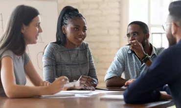 Group of colleagues having a discussion around a table in a modern office setting.