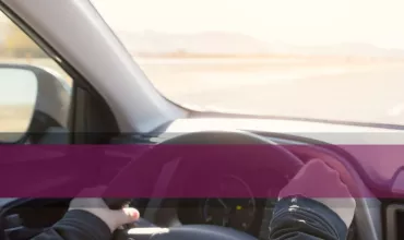 Person driving a car on a sunny day with a clear road ahead.