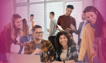 A group of people smiling and collaborating around a laptop in a bright office.